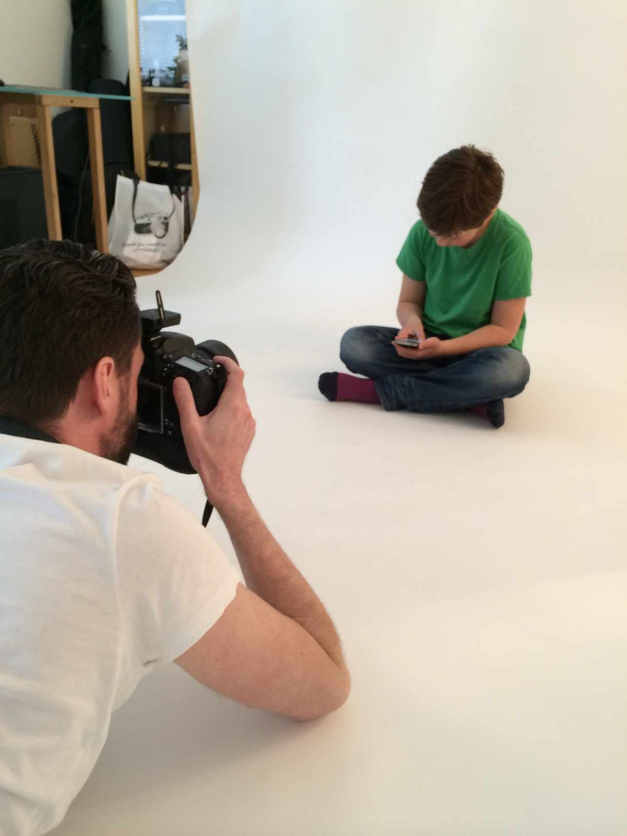 Fotograf som fotograferar en pojke i studiomiljö mot vit bakgrund, tillsammans med en skärm som visar pågående bildredigering, från produktionen av Sogetis bildbank