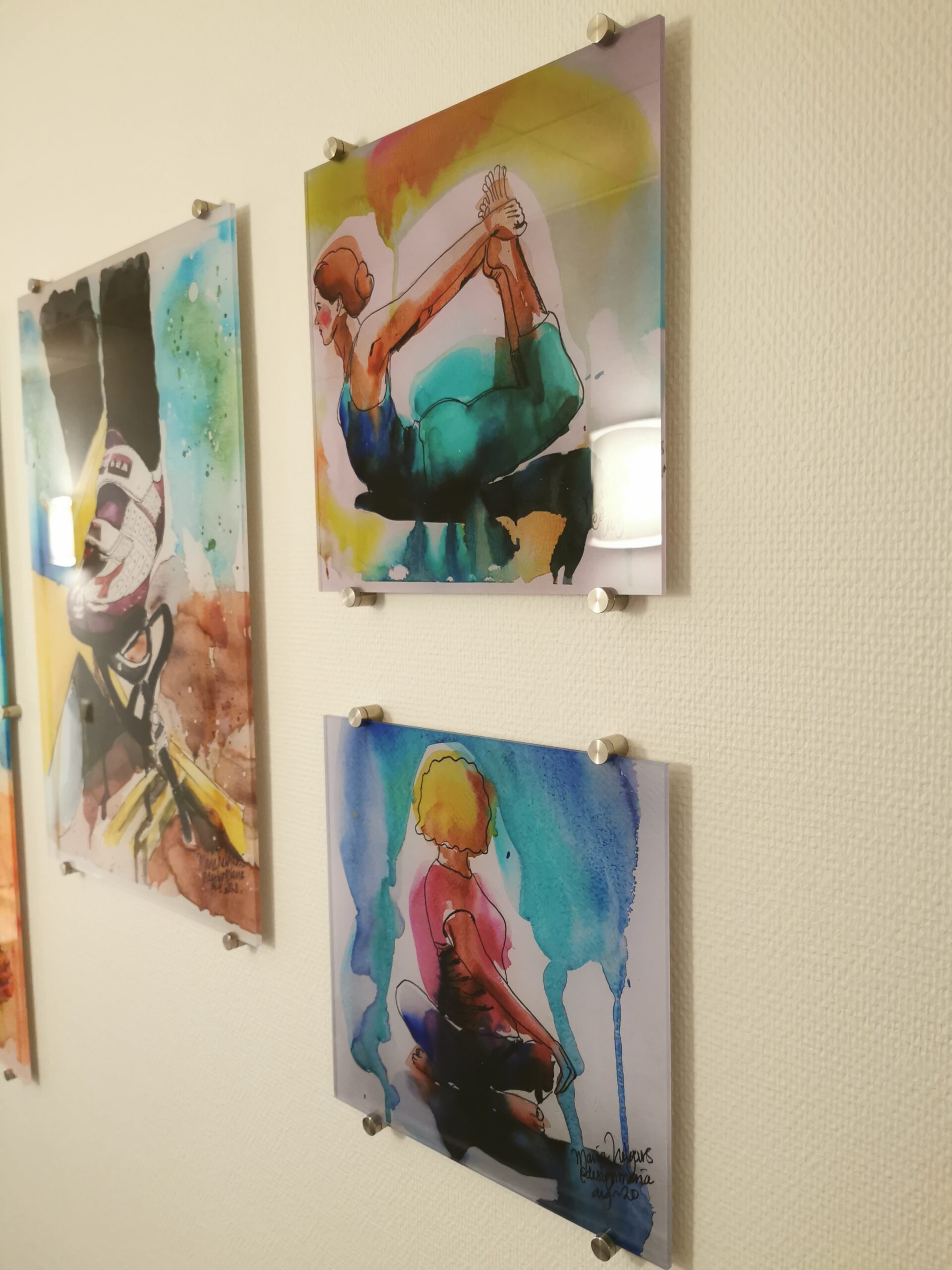 Tavlor till företag med akvarellmålade personer som yogar, i rörelse, en kvinna i bakåtböjning och en sittande figur i rosa och blått, uppsatta på Active Gyms vägg.